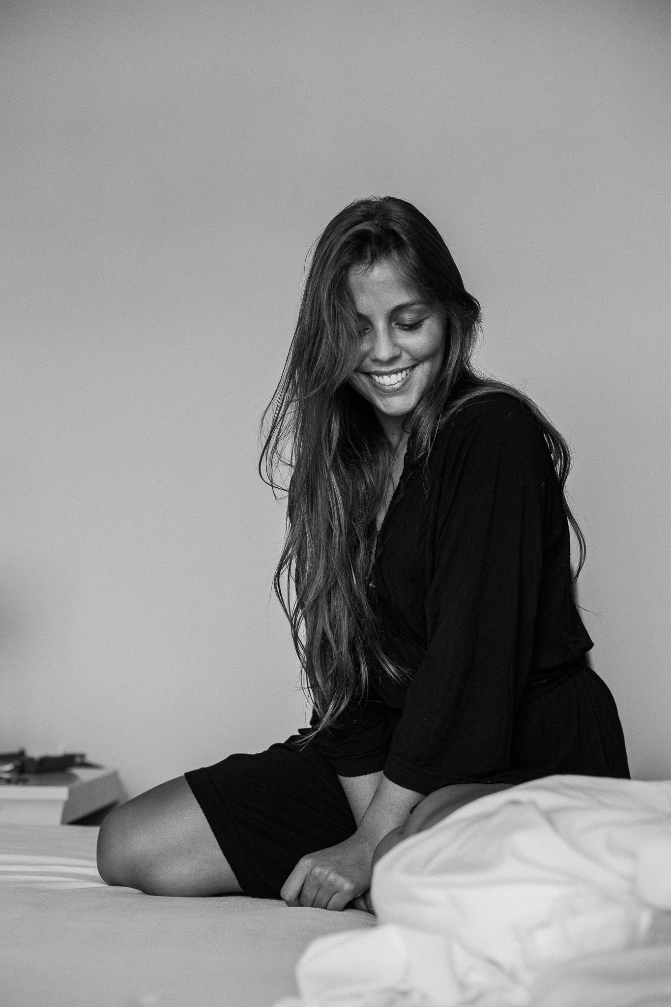 A black and white photo series shows a person in dark clothing lying on white bedding with long hair flowing.