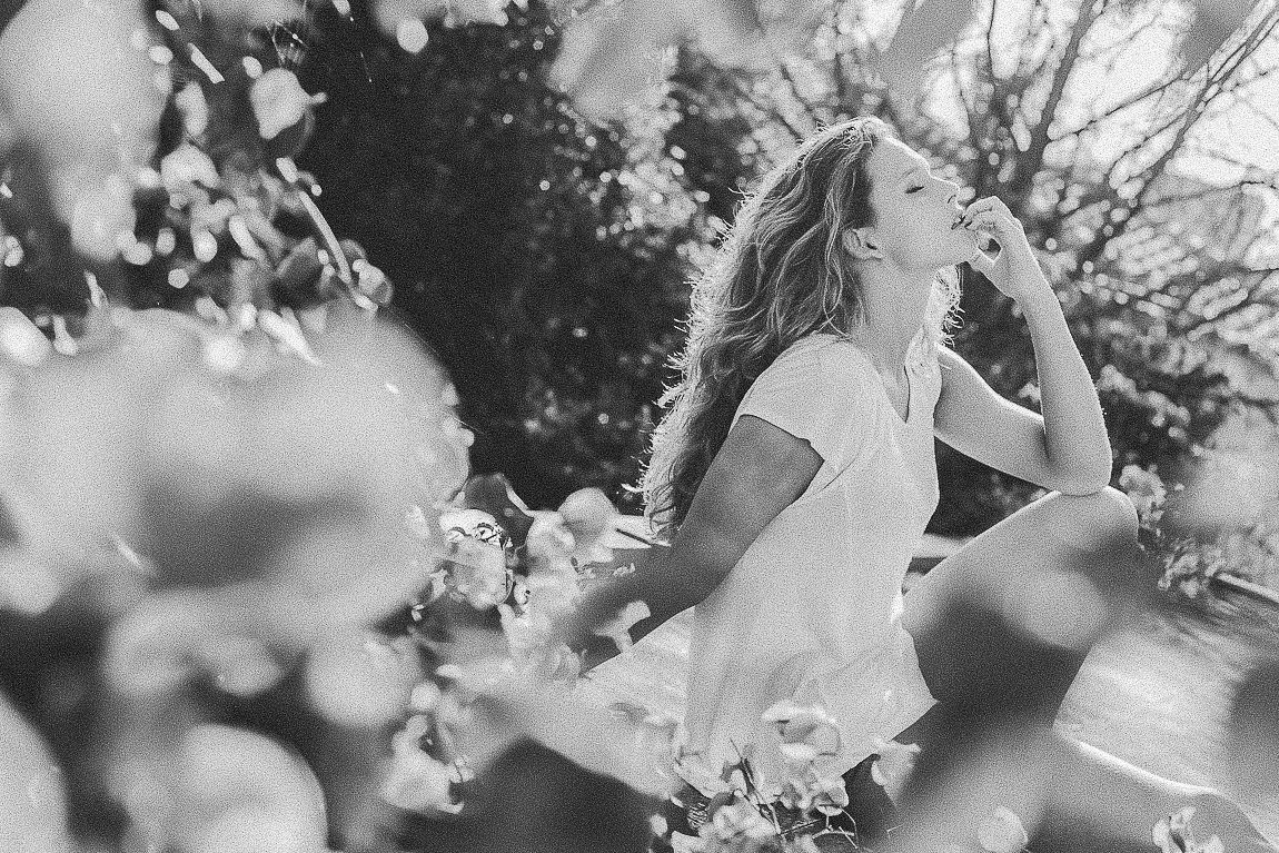 Bride and groom share a romantic kiss during their outdoor wedding ceremony surrounded by sunlit trees and flowers.