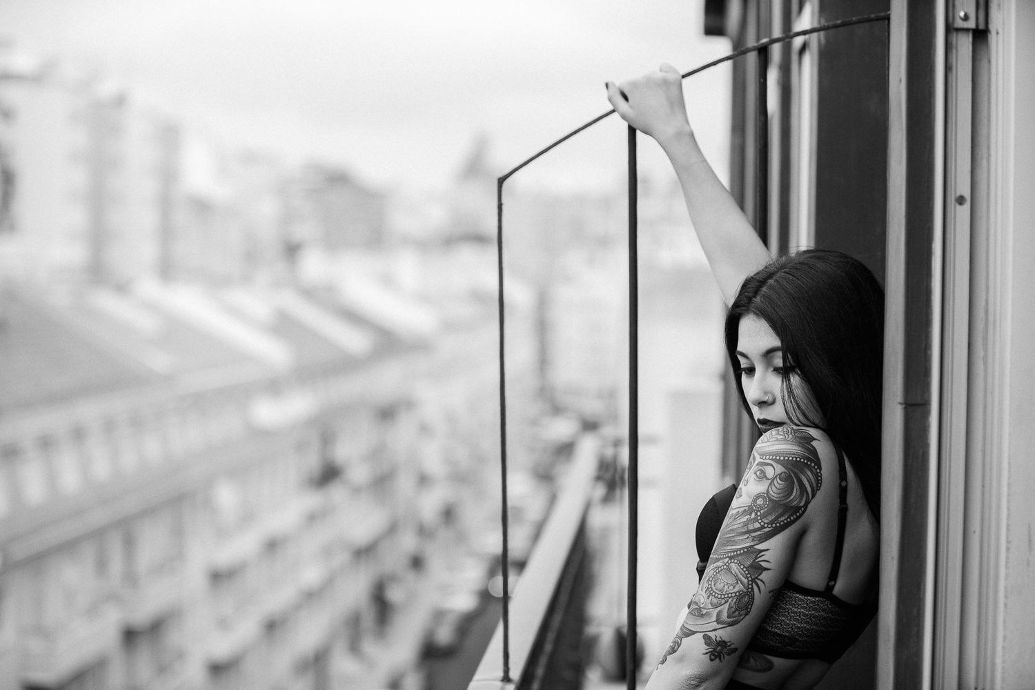 A silhouette gazes through an apartment window overlooking a cityscape in monochrome.