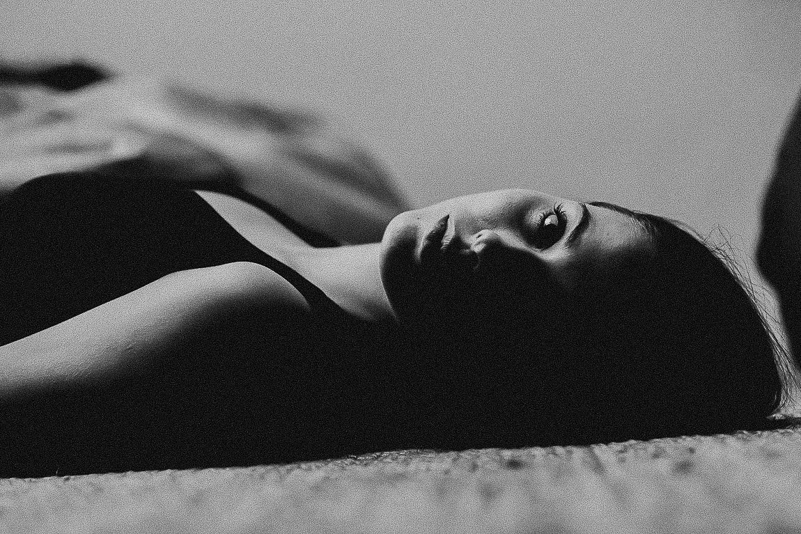 Black and white artistic photograph of a person reclining in a dramatic pose on a dark background.