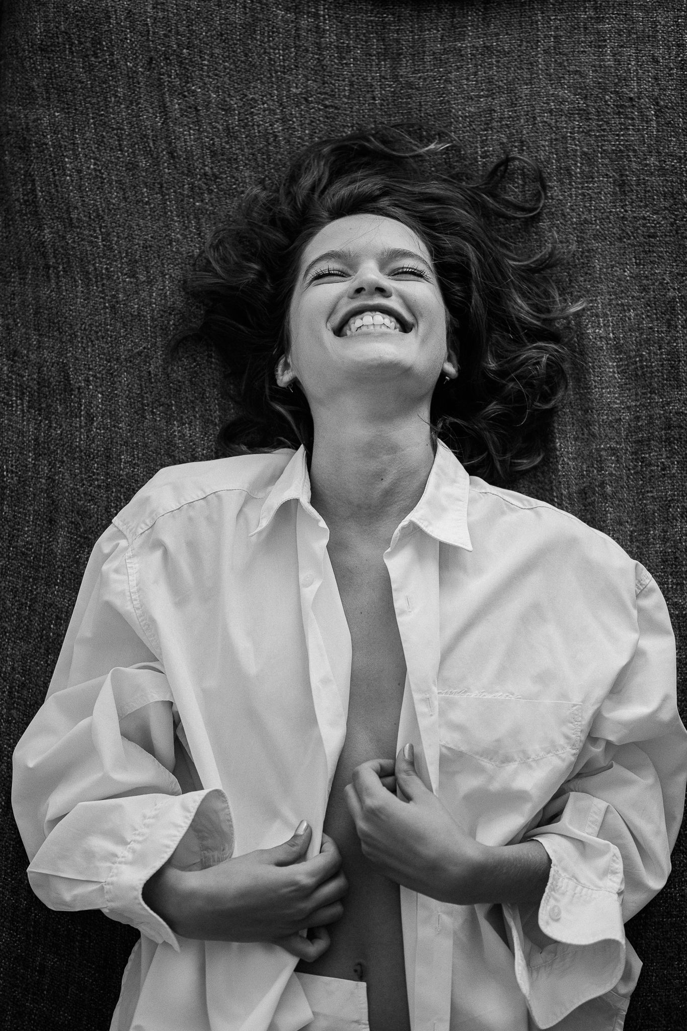 A series of black and white photos showing someone wearing a white shirt lying down and laughing expressively.