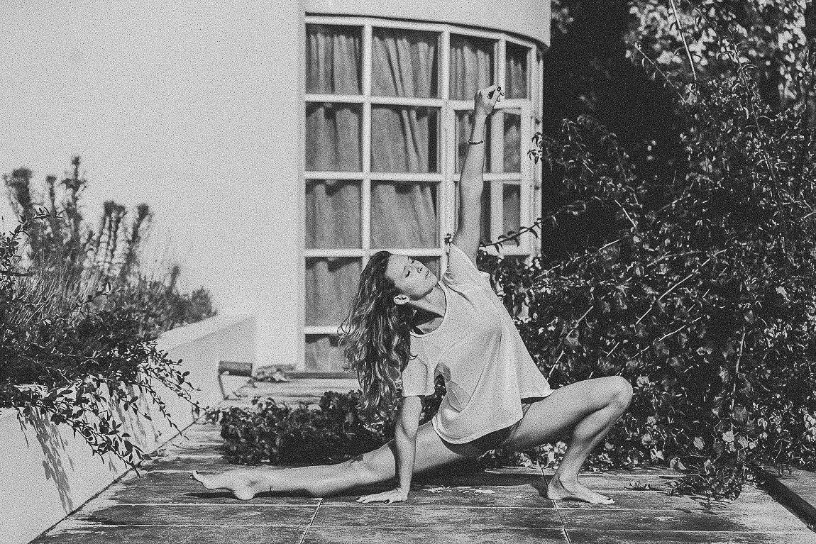 A black and white photograph shows a person lying in a relaxed pose on a windowsill of a vintage building.