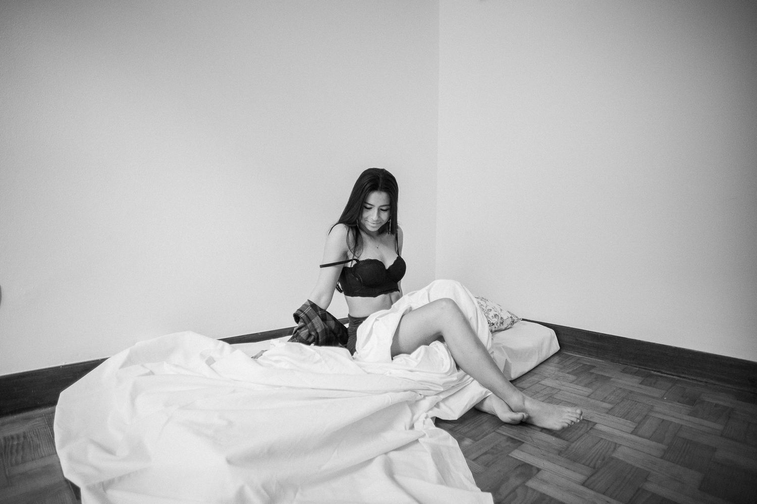 Black and white photograph of someone sitting on a hardwood floor against a white wall with fabric nearby.