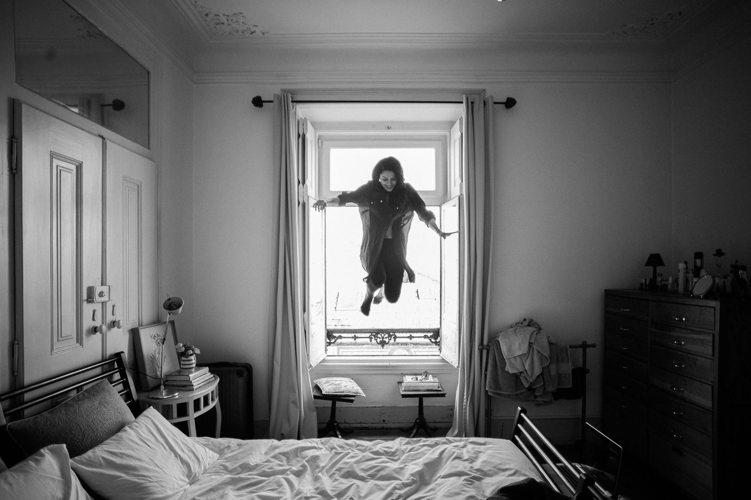 A black and white panoramic photo sequence showing a person jumping across windows in an interior space.