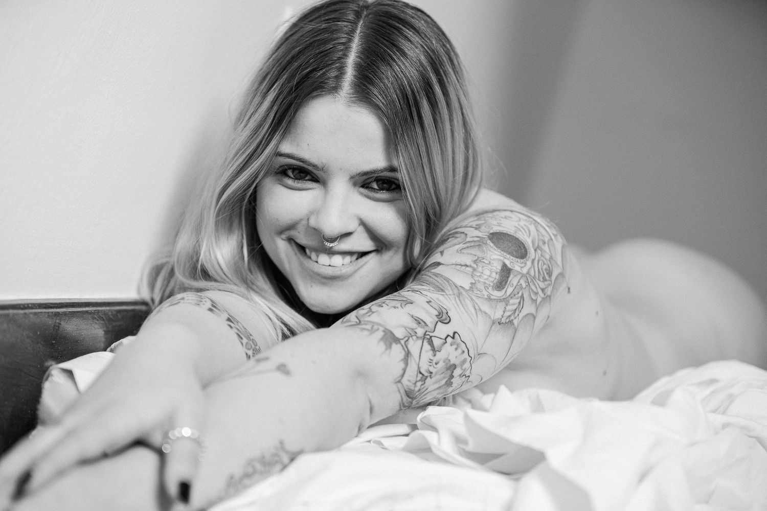 Black and white portrait series showing someone smiling while relaxing in bed with white linens and pillows.