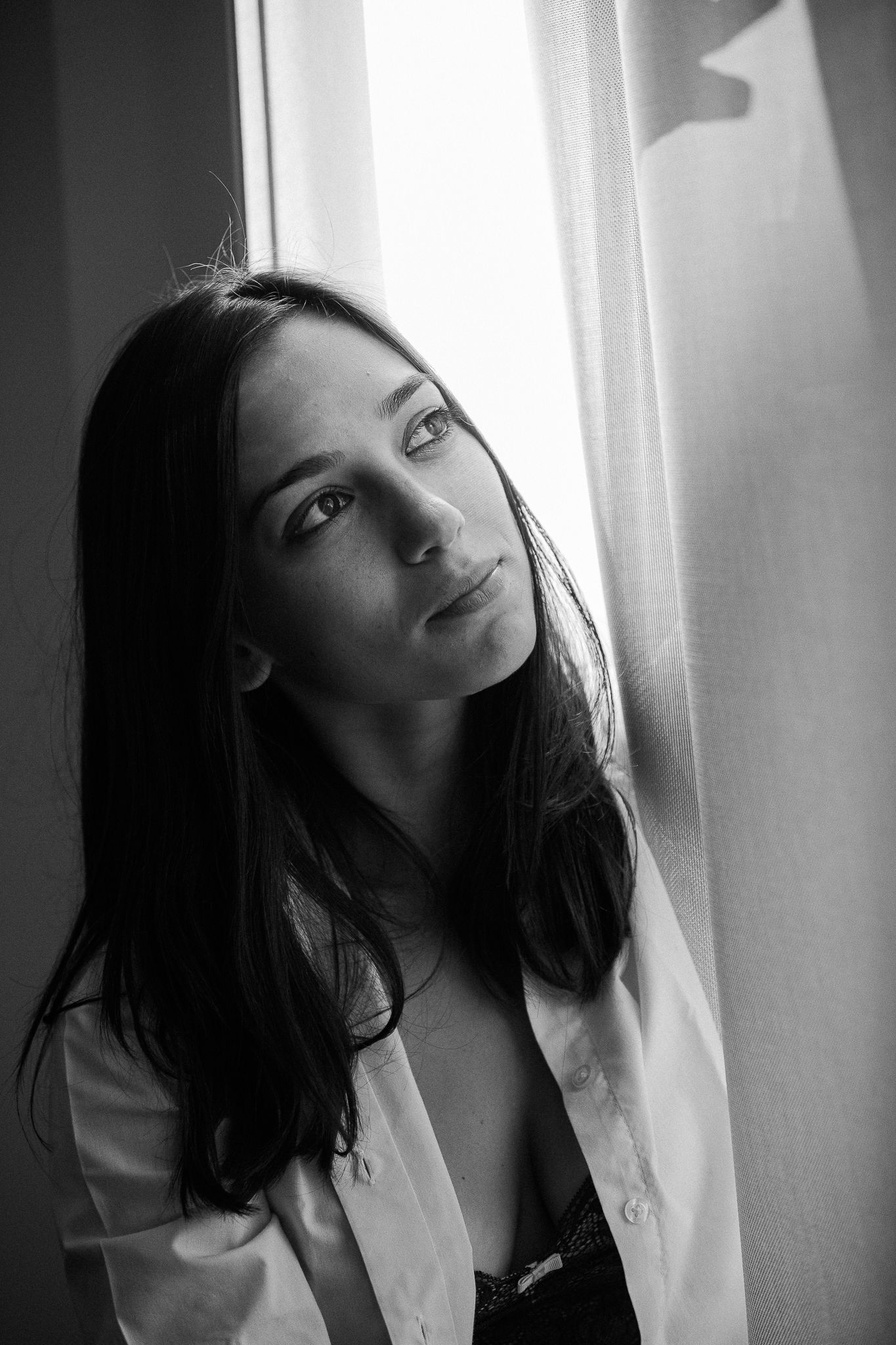 Black and white portrait series showing a person in a white shirt posing expressively against a bright window.