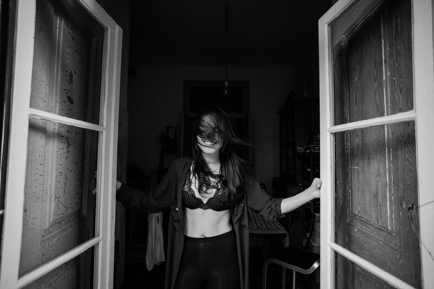 Black and white photo of a person peeking through an open window at night.