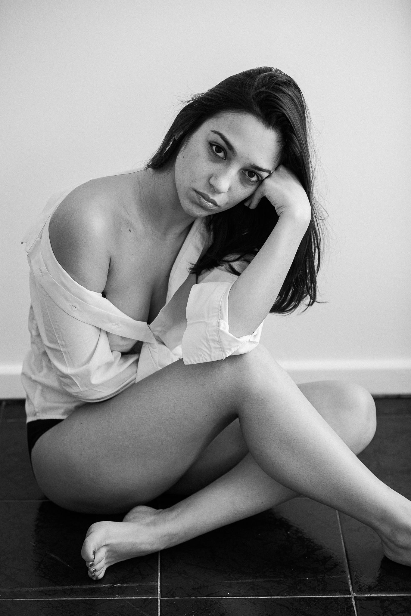 Black and white artistic portrait of a person sitting on tiled floor in an intimate pose.