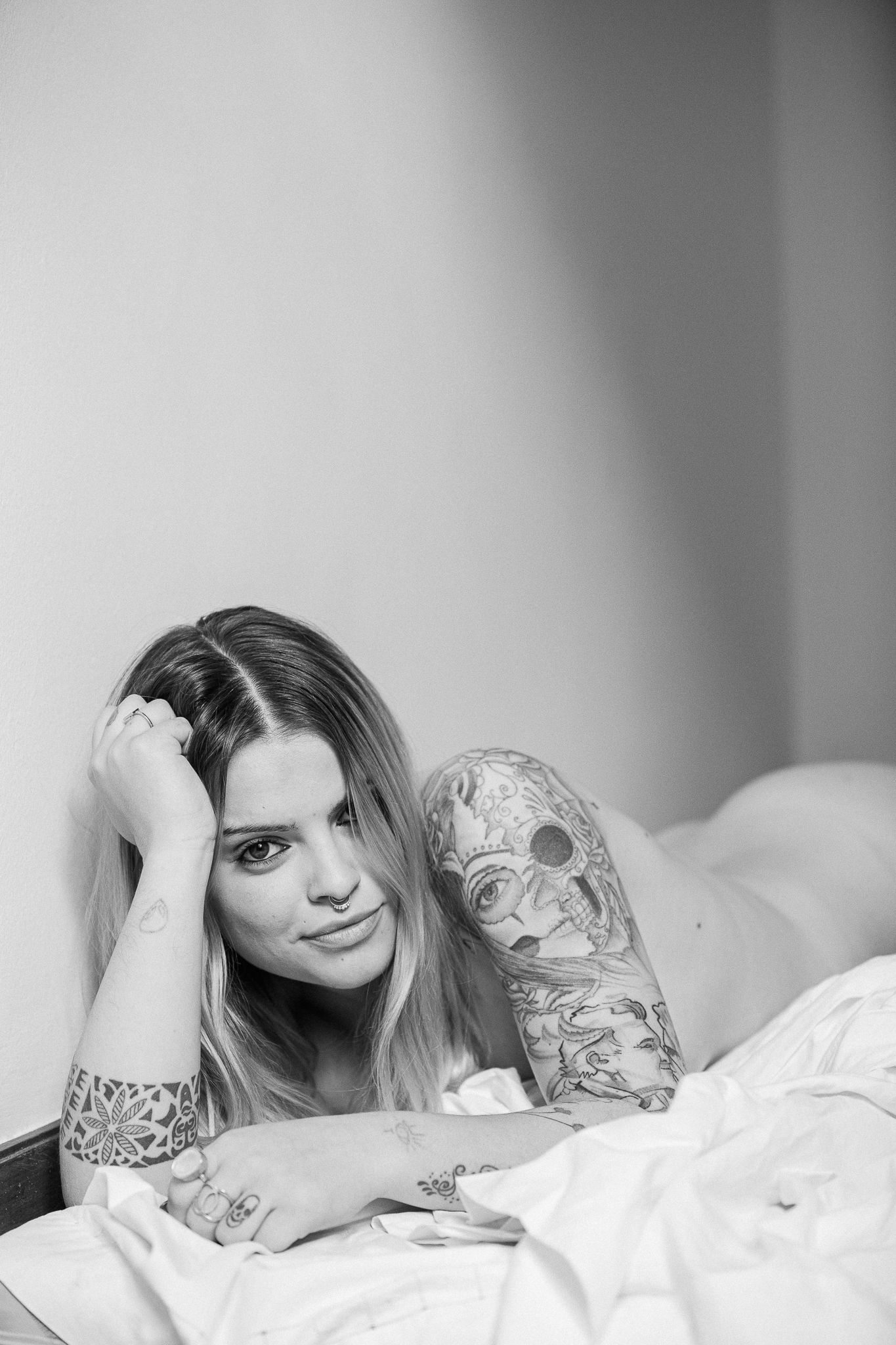 Black and white photo series showing a person with tattoos lying on white bedding in different relaxed poses.