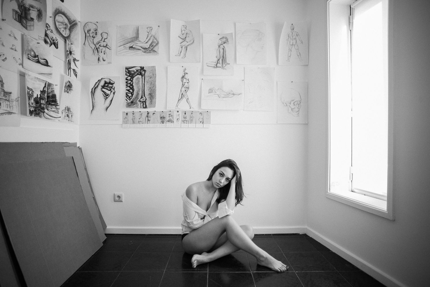 A black and white interior photograph showing sketches hung on walls in a bright room with natural lighting.