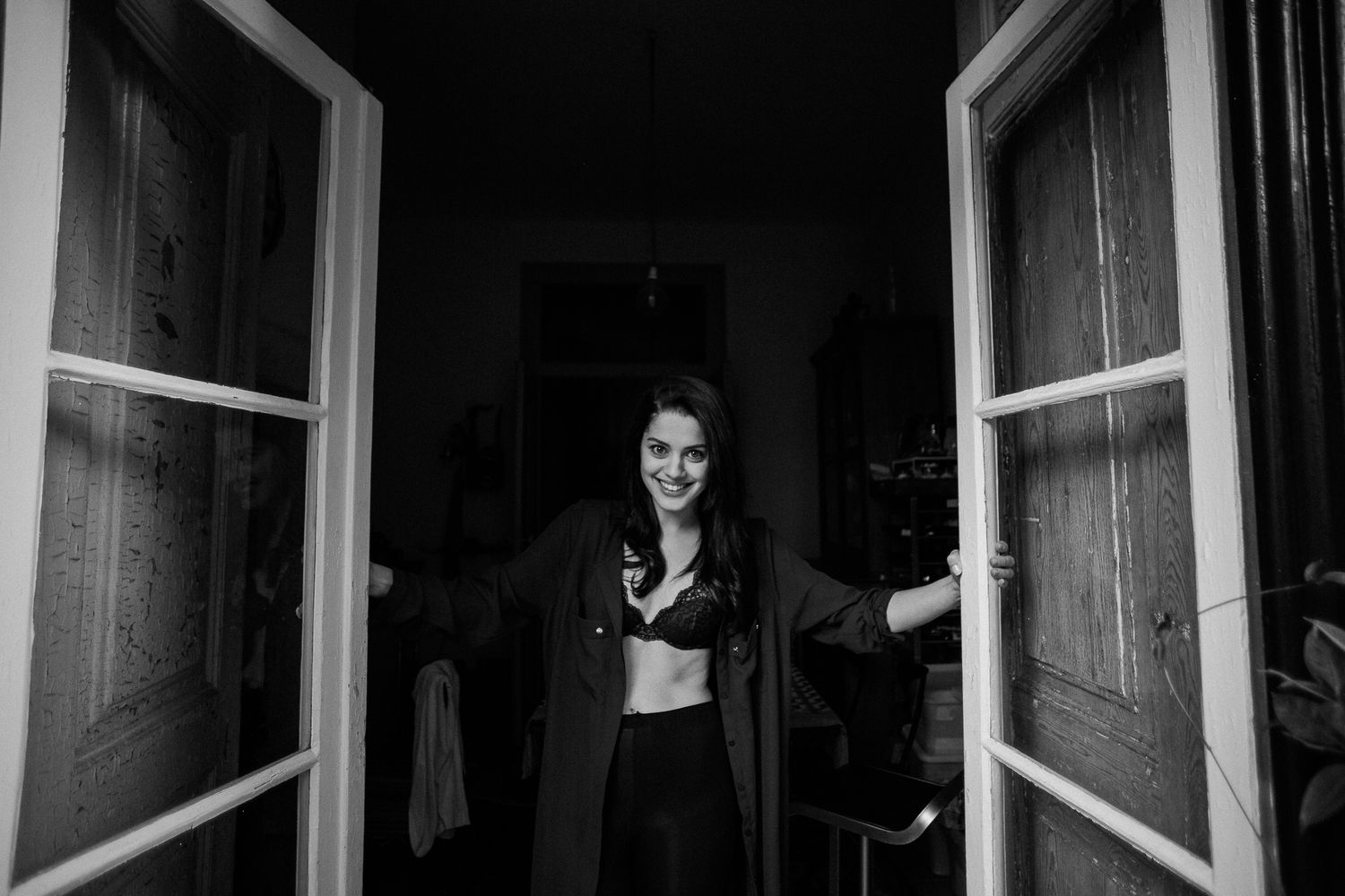 A person peers through an open window in a dramatic black and white photograph.