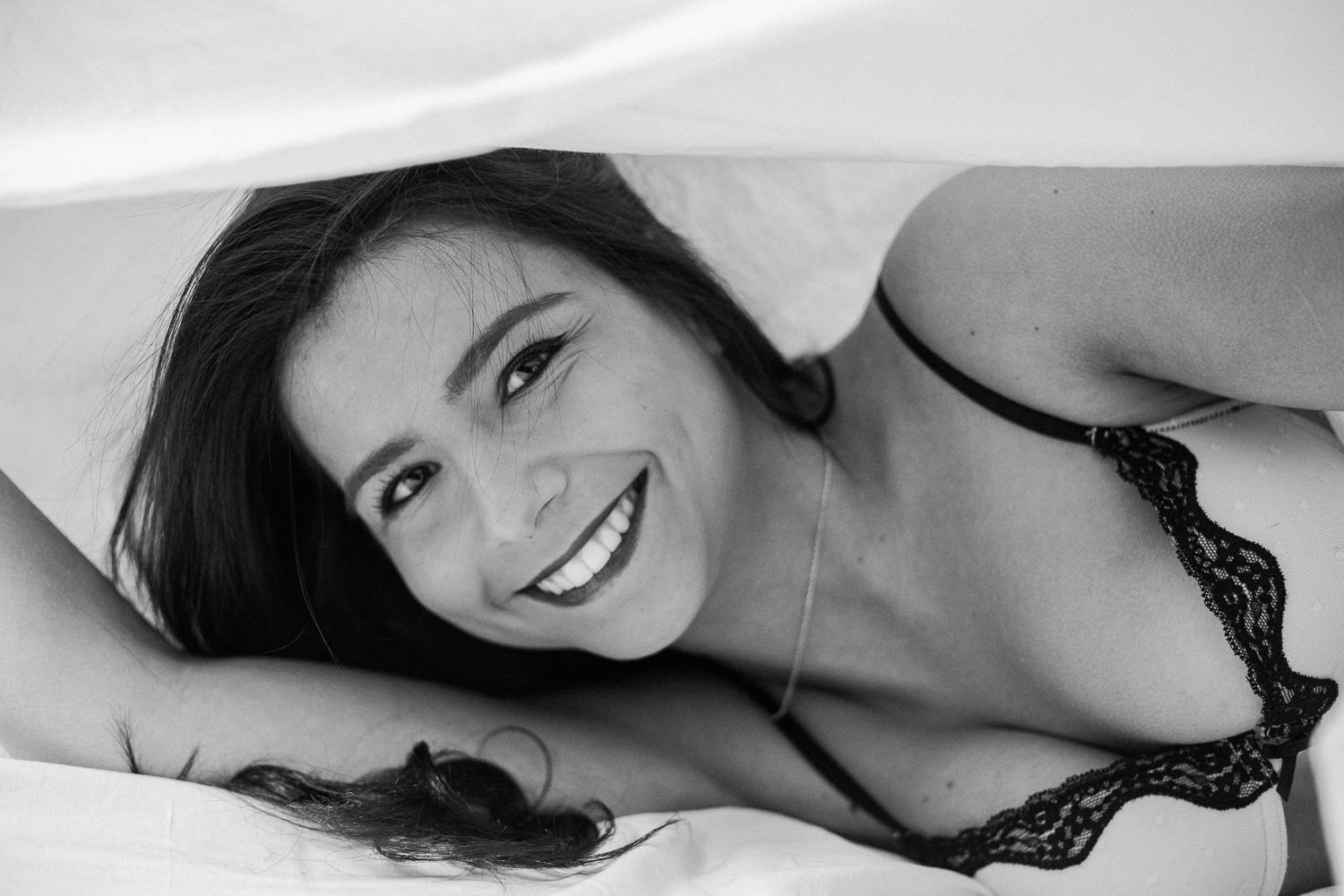 A series of black and white boudoir photos showing intimate poses against white bedding.