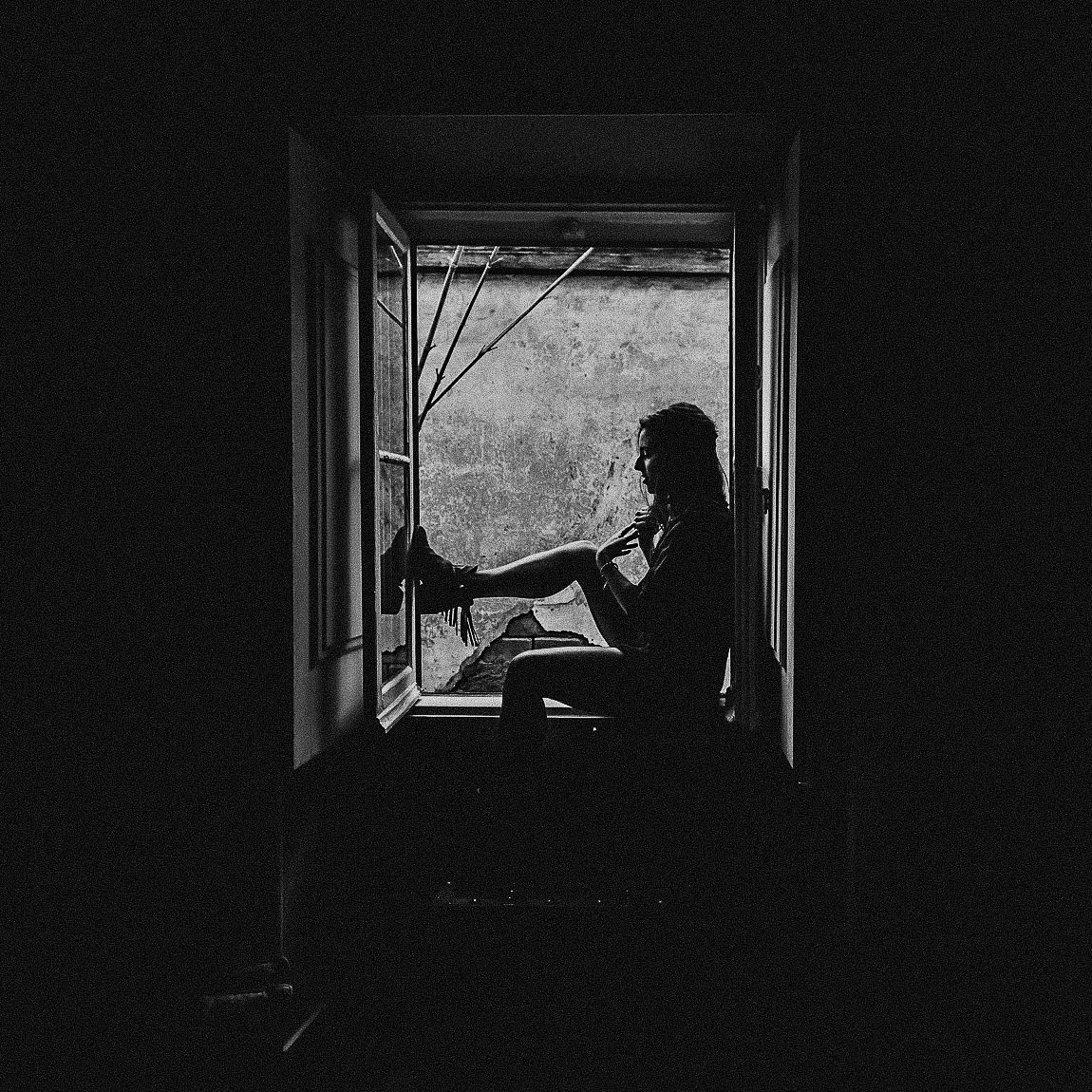 Dark silhouette of a person standing in a doorway against bright backlighting in a moody black and white scene.