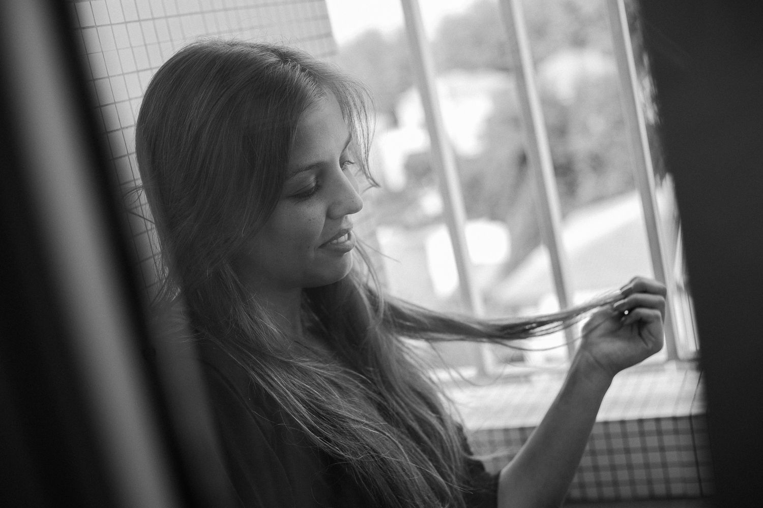 A black and white photo series showing a woman with long hair looking out a window in various contemplative poses.