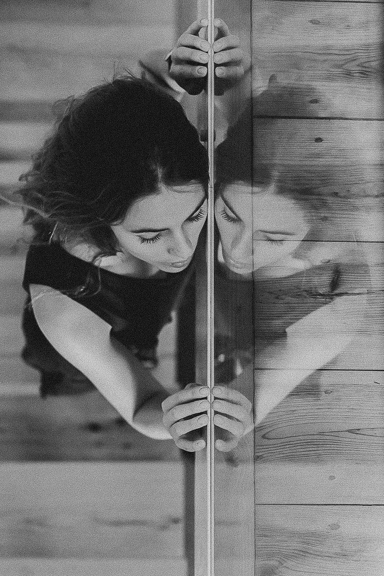 Artistic black and white portrait of someone peeking through wooden slats, creating a dramatic shadow effect.