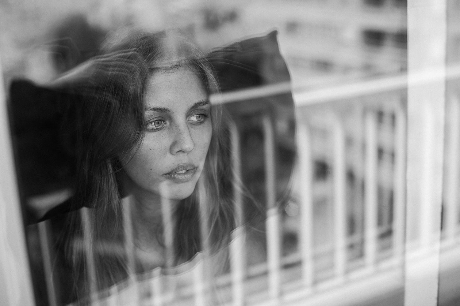 Black and white portrait of woman with long hair looking through window reflection.