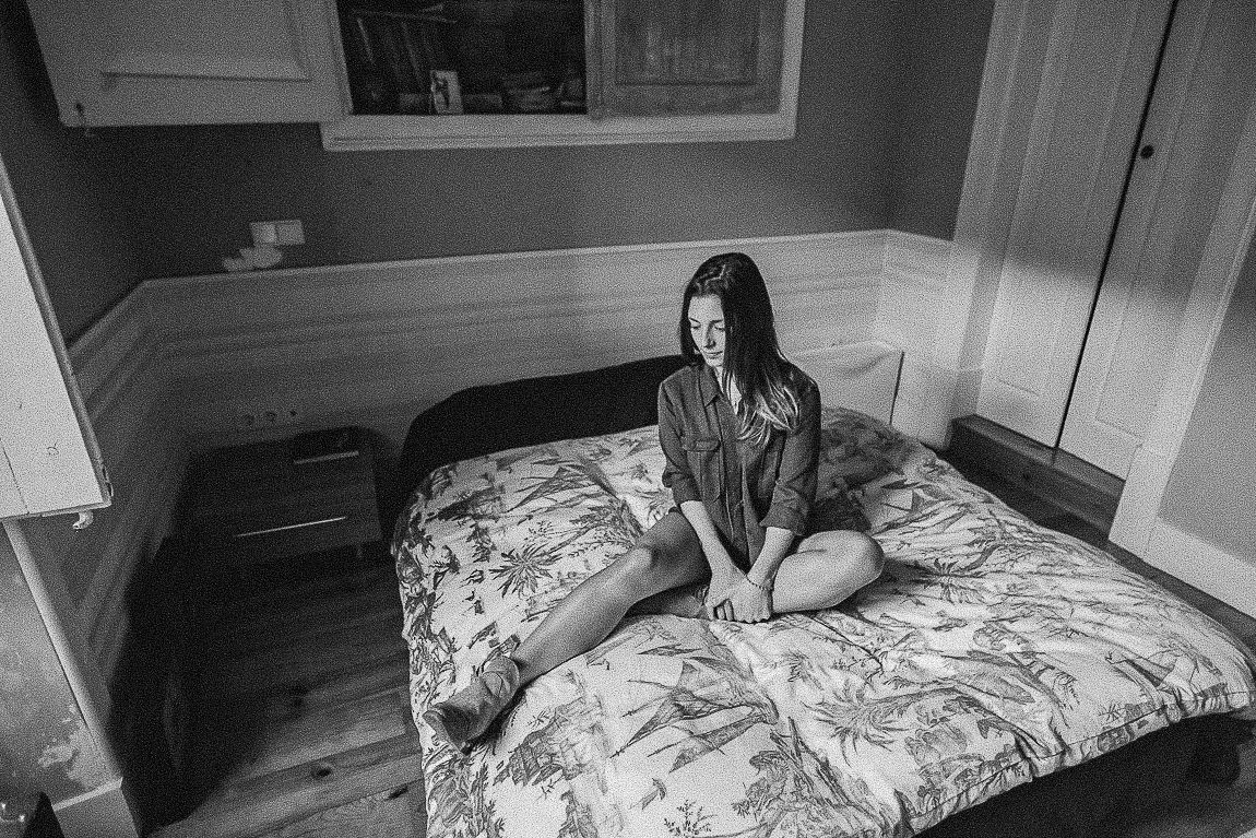 Black and white photograph showing a messy unmade bed with rumpled sheets and blankets.