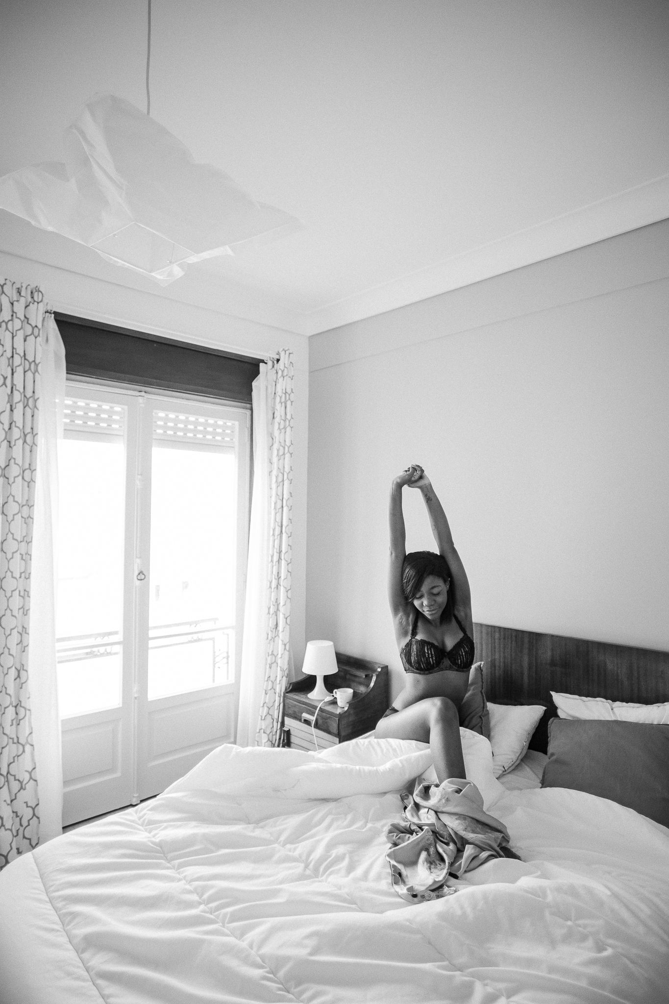 A sequence of black and white photos showing someone relaxing and stretching on a white bed in a bright bedroom.