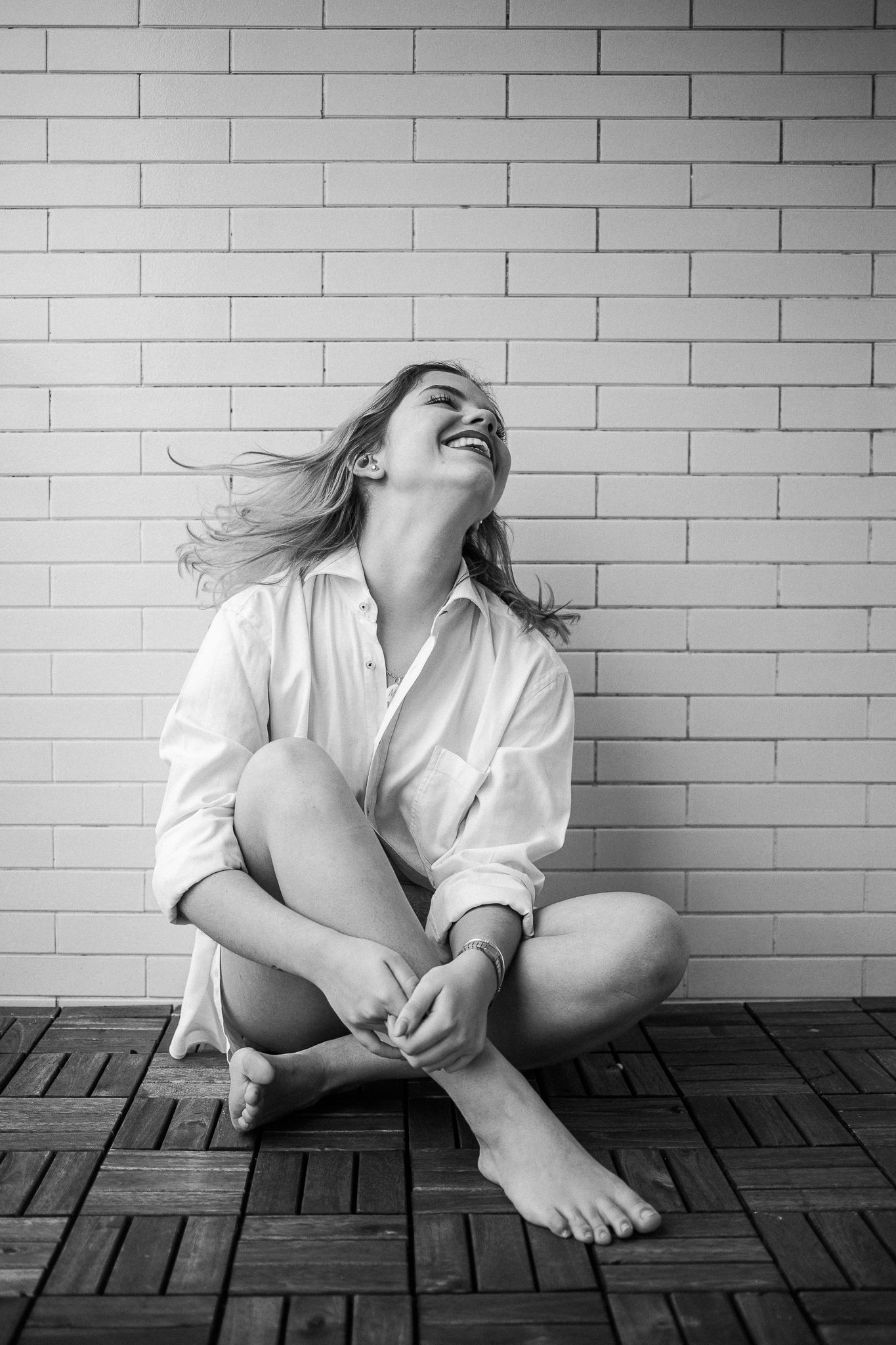 A series of black and white photos showing someone in a white shirt sitting against a brick wall on wooden flooring.