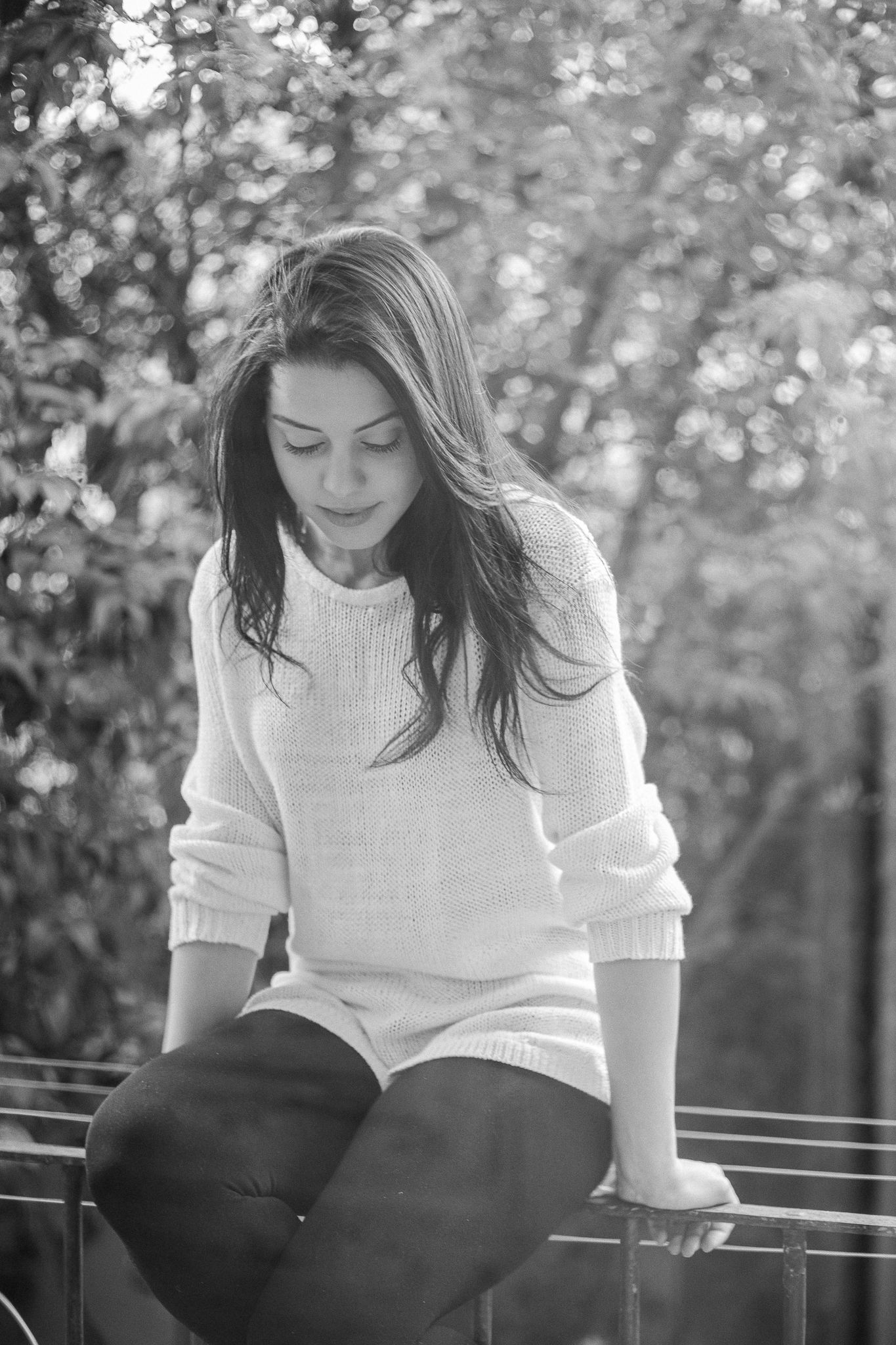 Black and white portrait of someone in a cozy white sweater sitting outdoors with soft bokeh background.