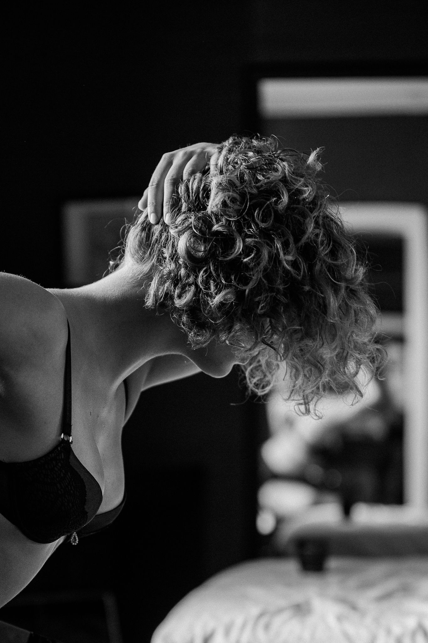 Black and white artistic photograph of curly hair silhouetted against a dark background.
