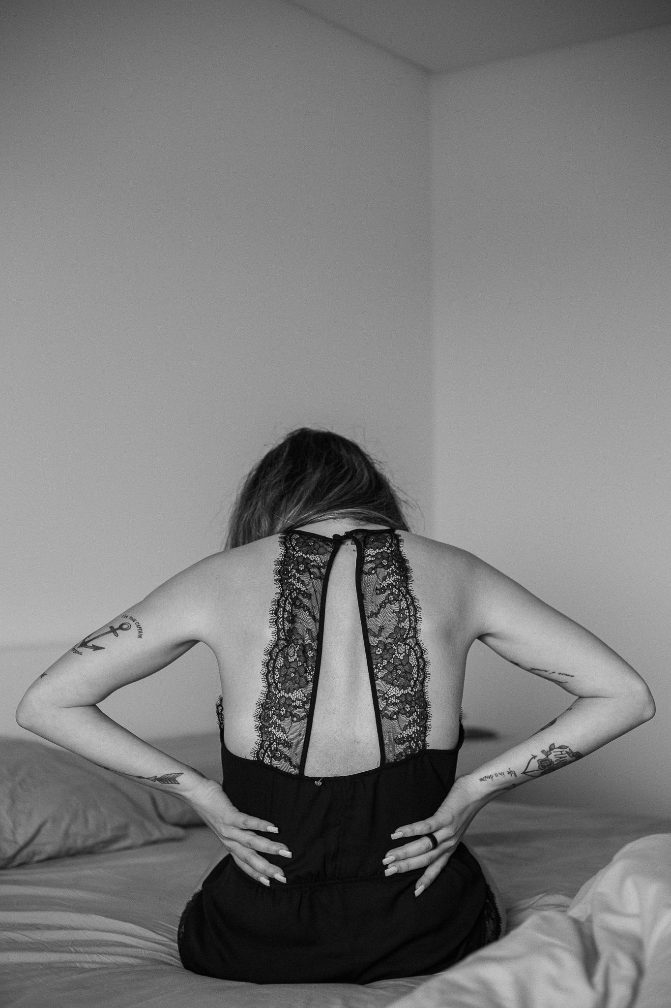 Black and white photo of someone in dark lingerie reclining on white bedding.