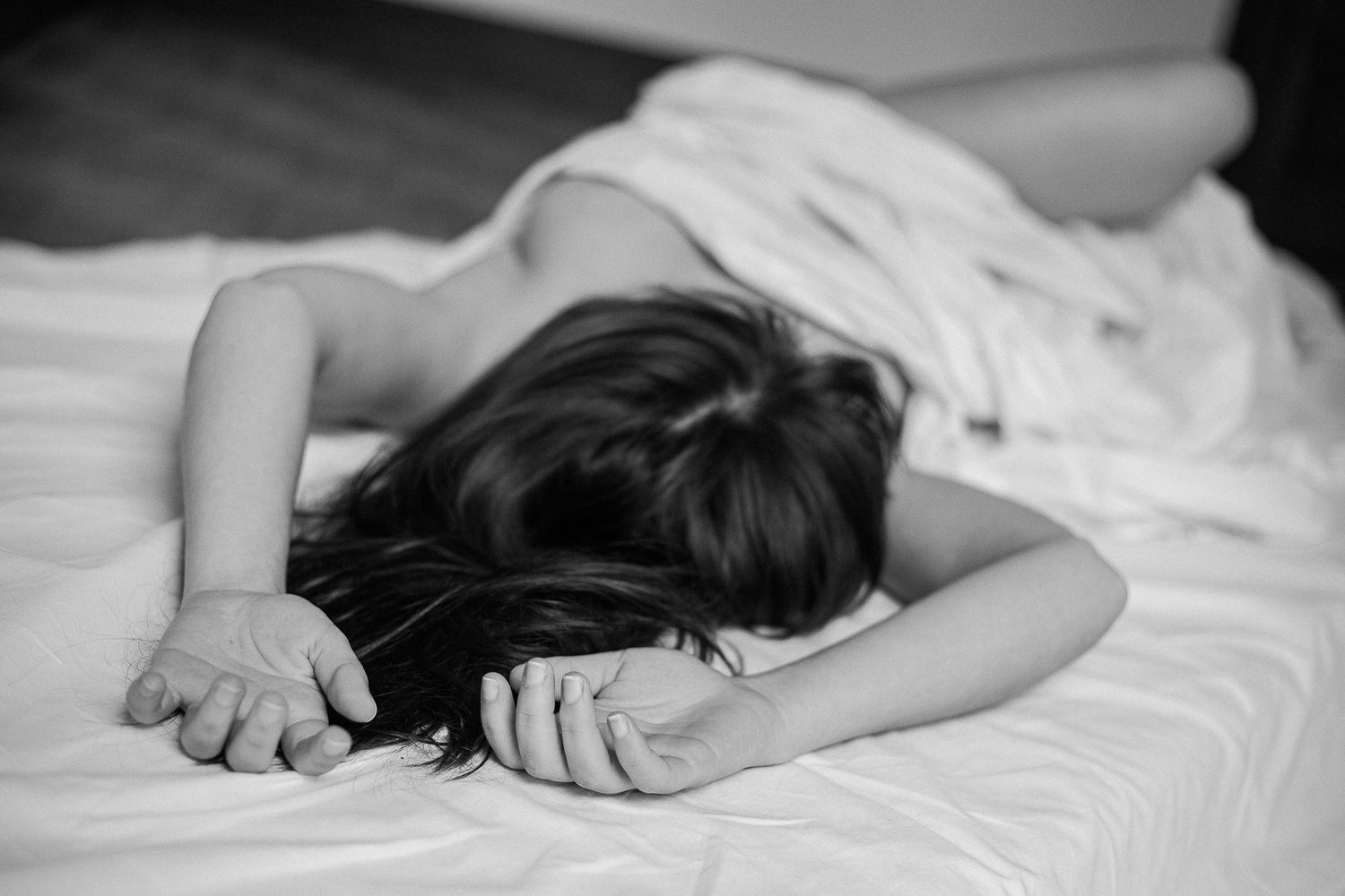 Black and white artistic photo showing someone resting on white bedding.