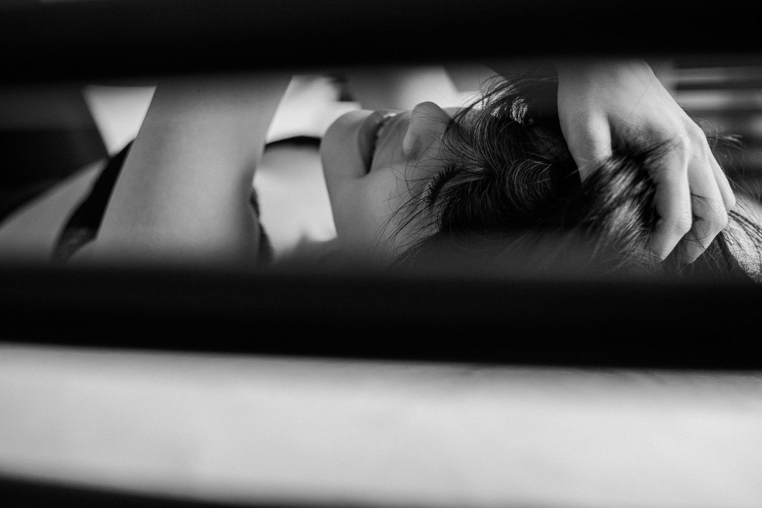 Black and white artistic portrait showing a person resting in dramatic light and shadow between horizontal lines.