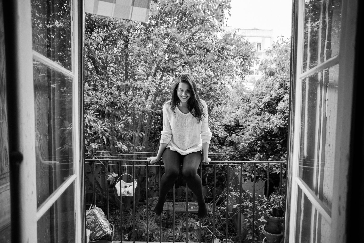 Black and white photo of a couple in a romantic moment near a window with natural light streaming in.