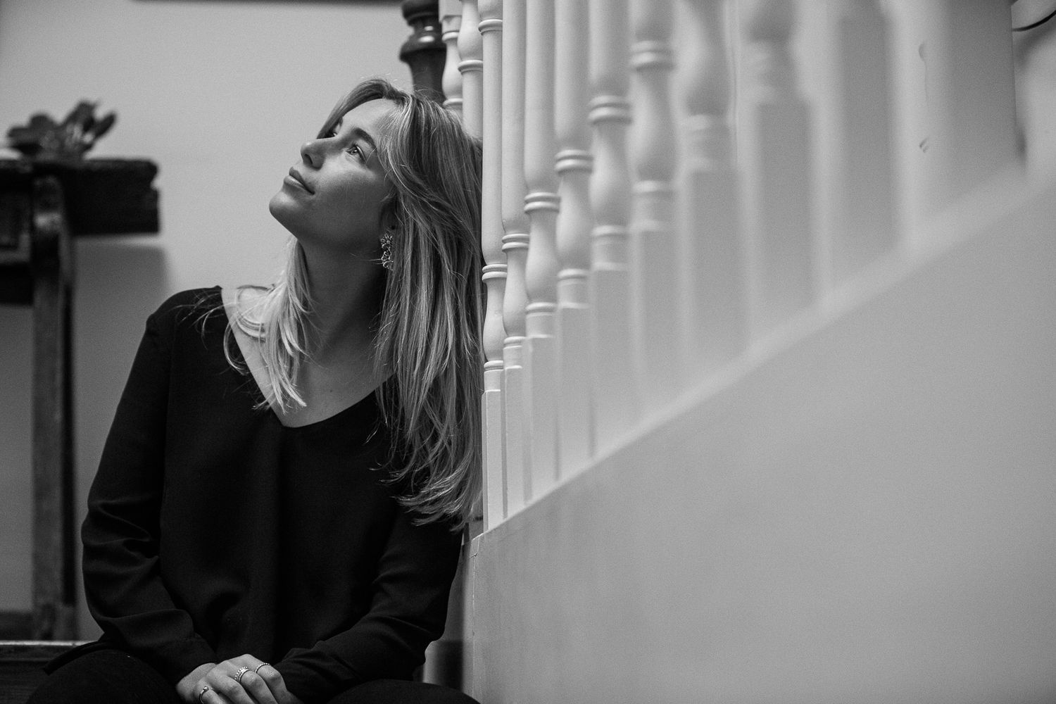 Person in black sweater sits on white stairs while looking down pensively in a dramatic black and white portrait.