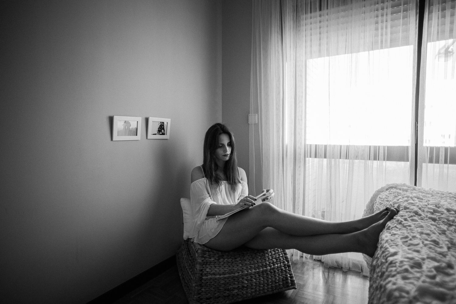 A person sits relaxed in a wicker chair by a window, reading in a moody black and white setting.