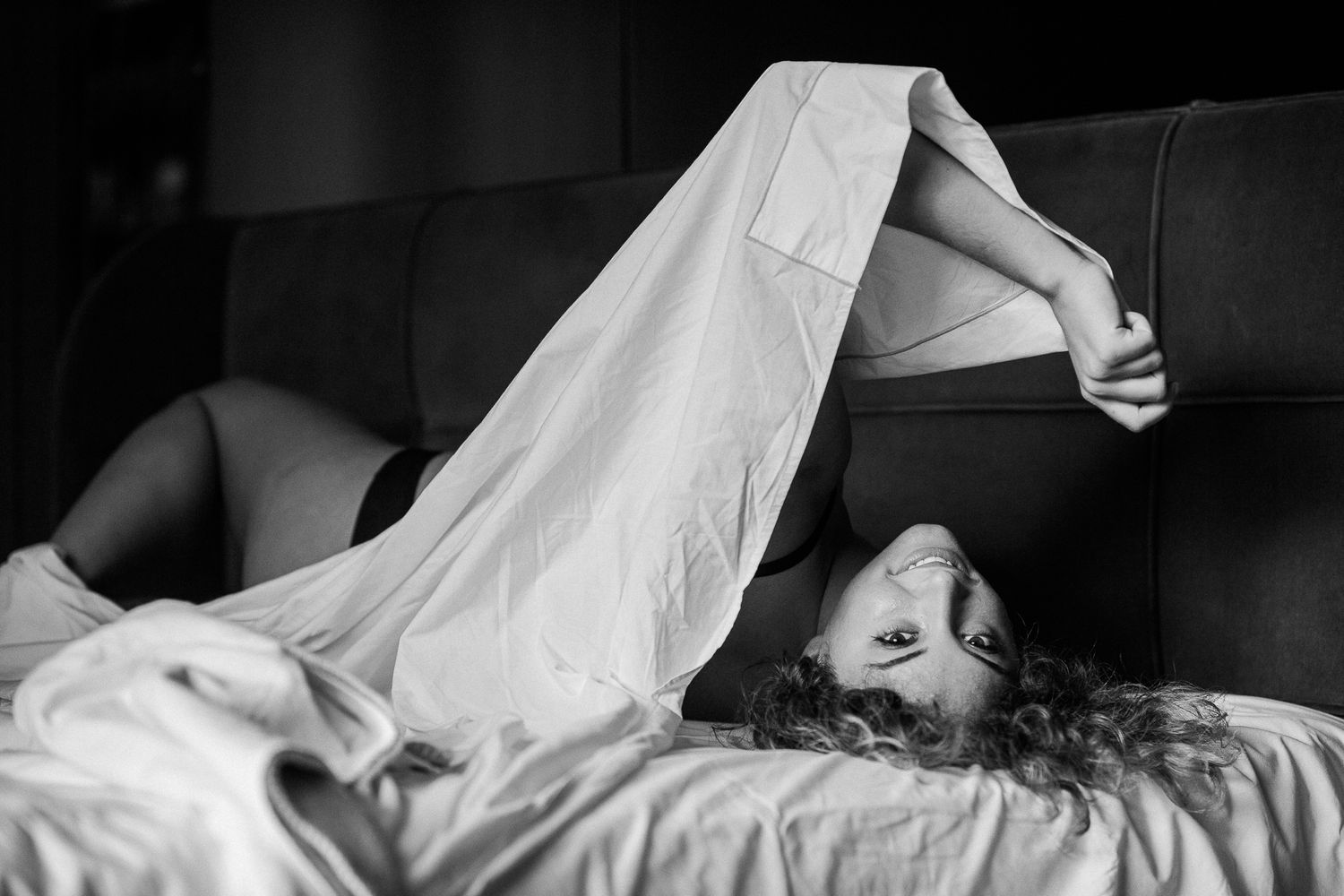 Black and white photo of someone sleeping peacefully under white bedsheets in soft morning light.