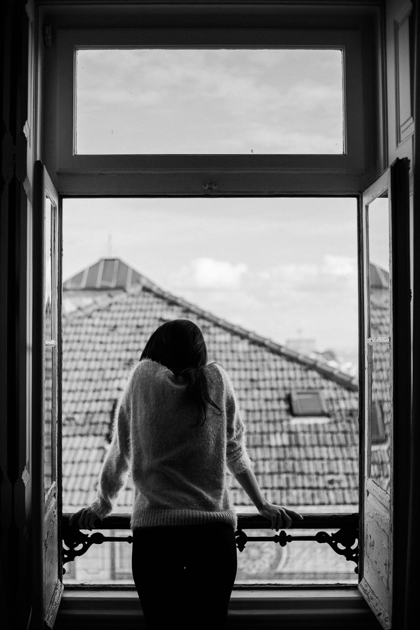 Three black and white photographs show silhouettes of people looking out windows at tiled rooftops in the distance.