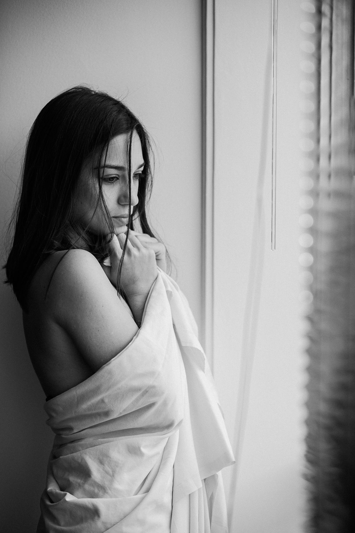 A black and white photo series showing a person wrapped in white fabric against a window with dramatic lighting.