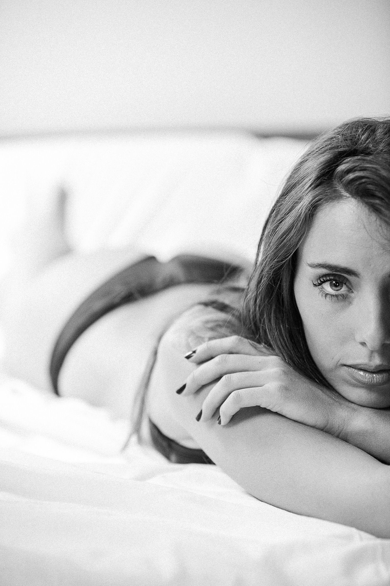 Intimate black and white portrait series showing gentle poses on white bedding.