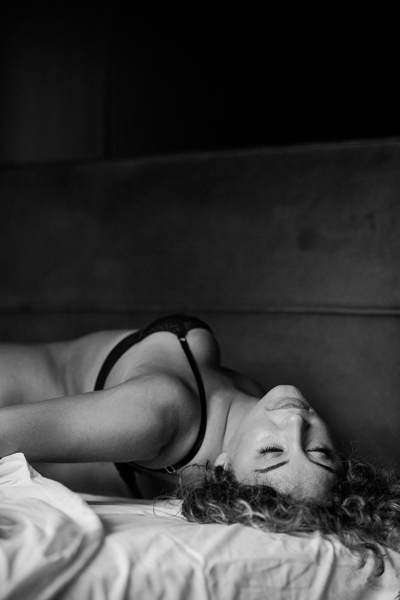 A person lies sleeping peacefully in bed with dark curly hair against white bedding in black and white tones.