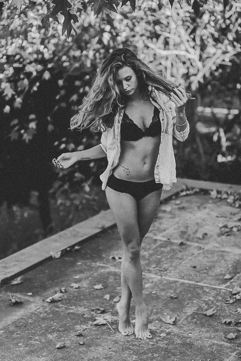 Black and white artistic portrait of a figure in swimwear and open shirt dancing outdoors in a natural setting.