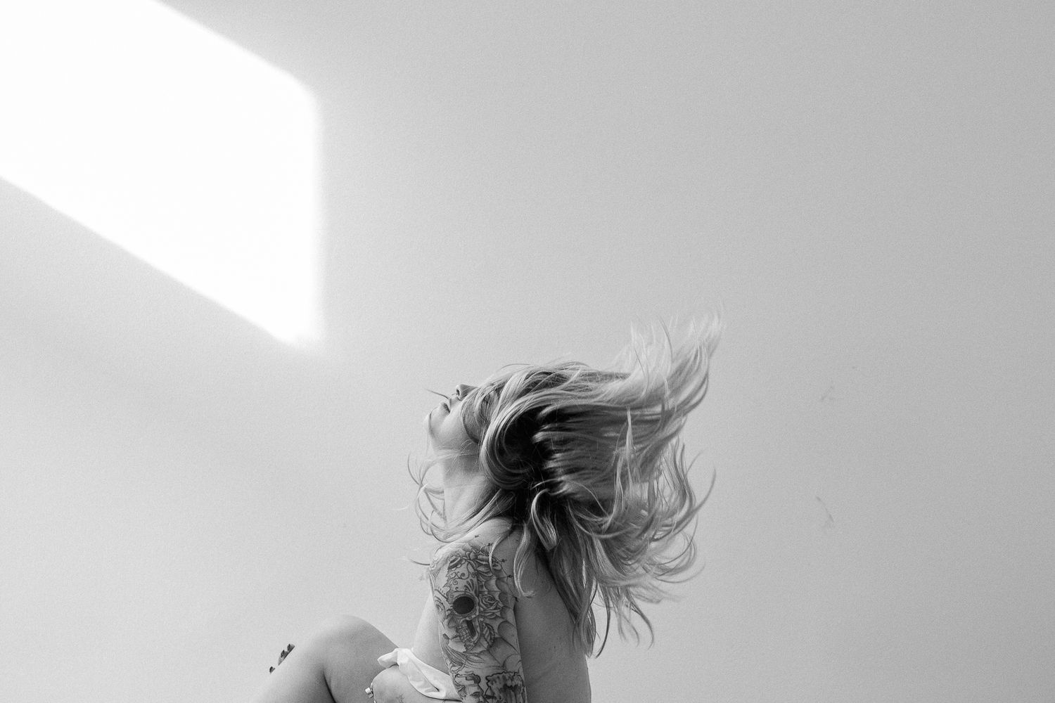 Black and white photo showing hair flipping dramatically against a stark white wall in an artistic motion shot.