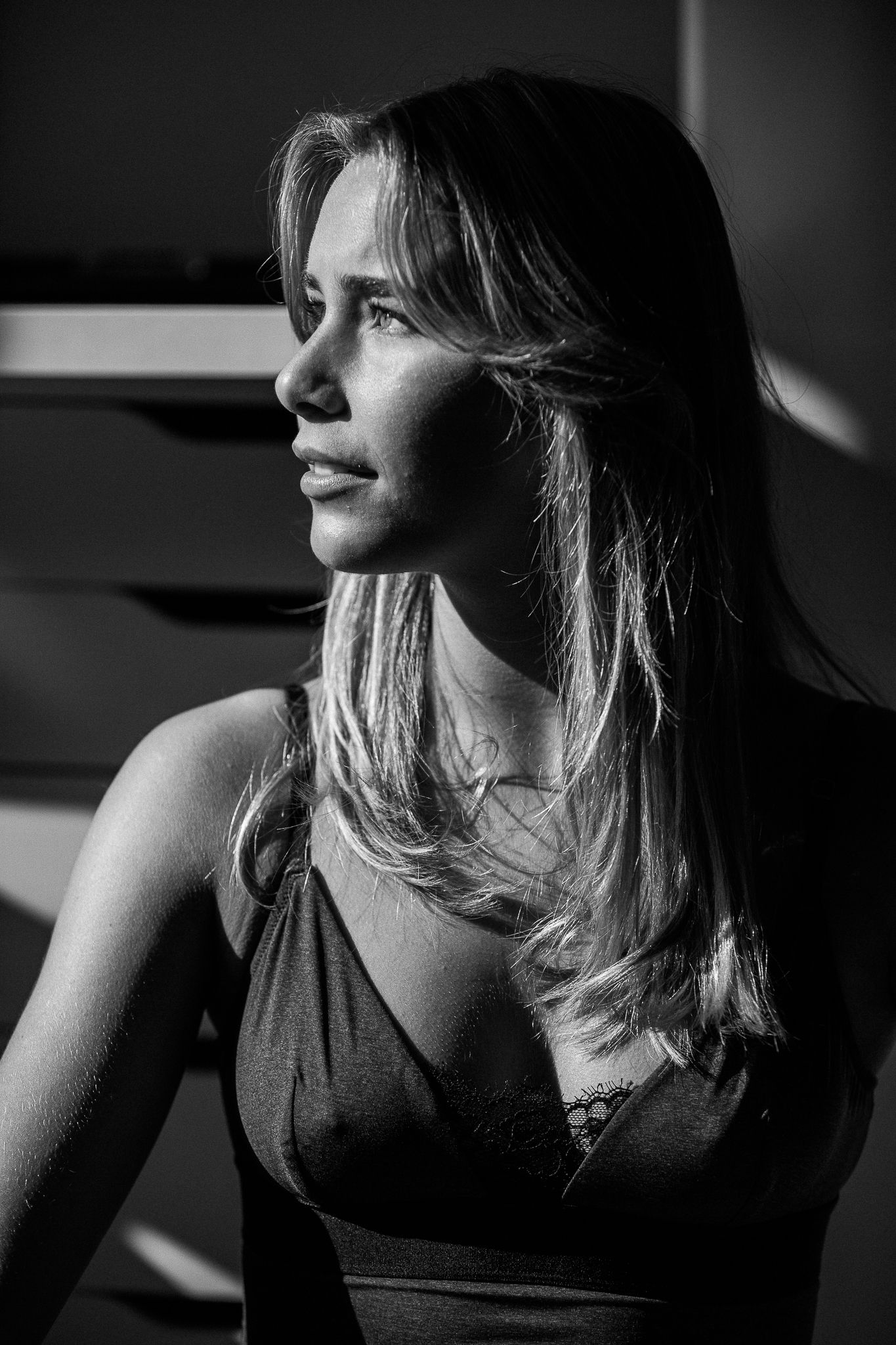 Dramatic black and white portrait of a woman in profile with windswept hair and a dark top against moody lighting.