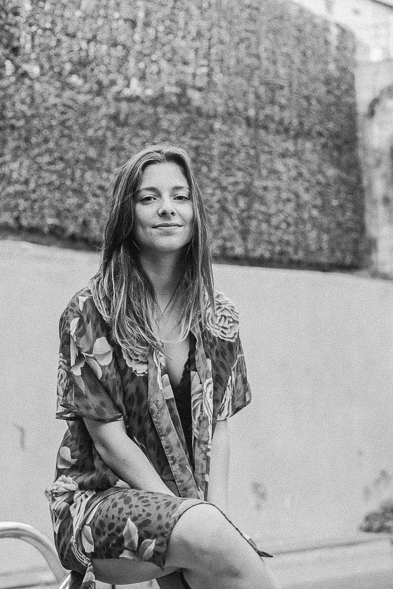 Black and white photo series showing a person in a floral print dress sitting outdoors against a textured stone wall.