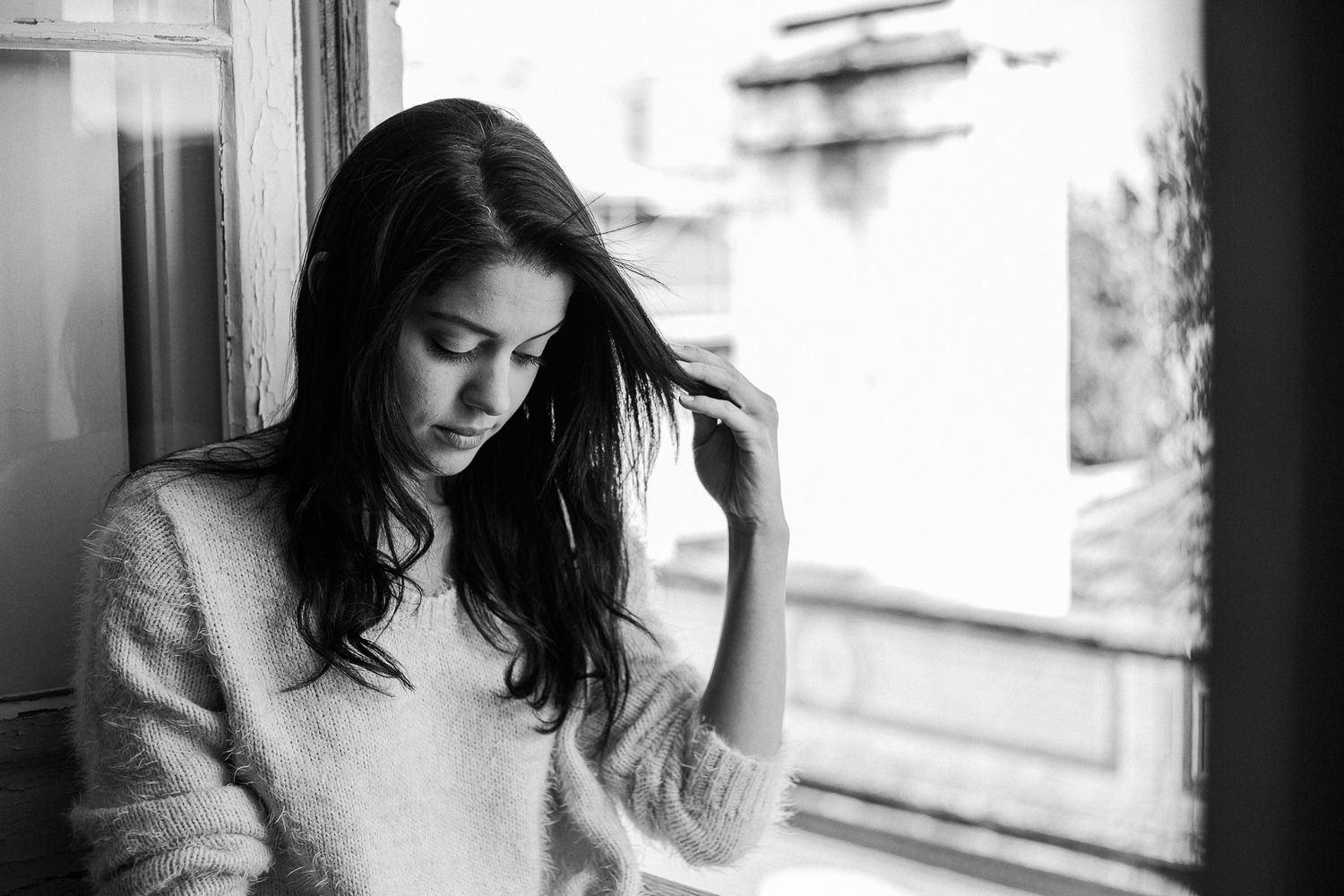 A black and white photo series showing someone looking down pensively near a window in moody lighting.