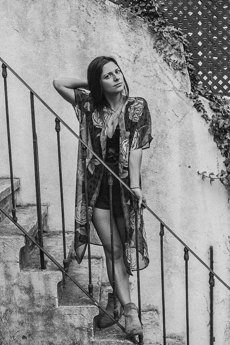 Black and white portrait of a person in a patterned kimono robe posing on outdoor stone steps against a textured wall.