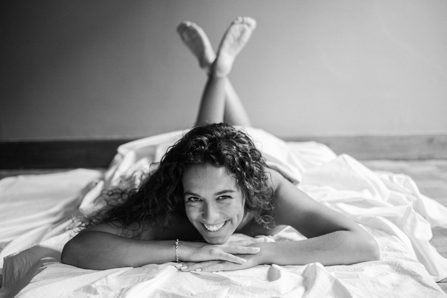 A black and white artistic portrait series showing someone lying on white bedding in various relaxed poses.