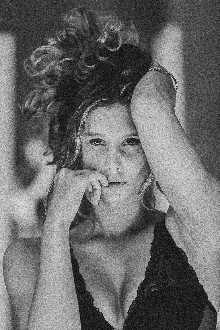 Black and white portrait of a person with curly hair wearing a lace top in an artistic pose.