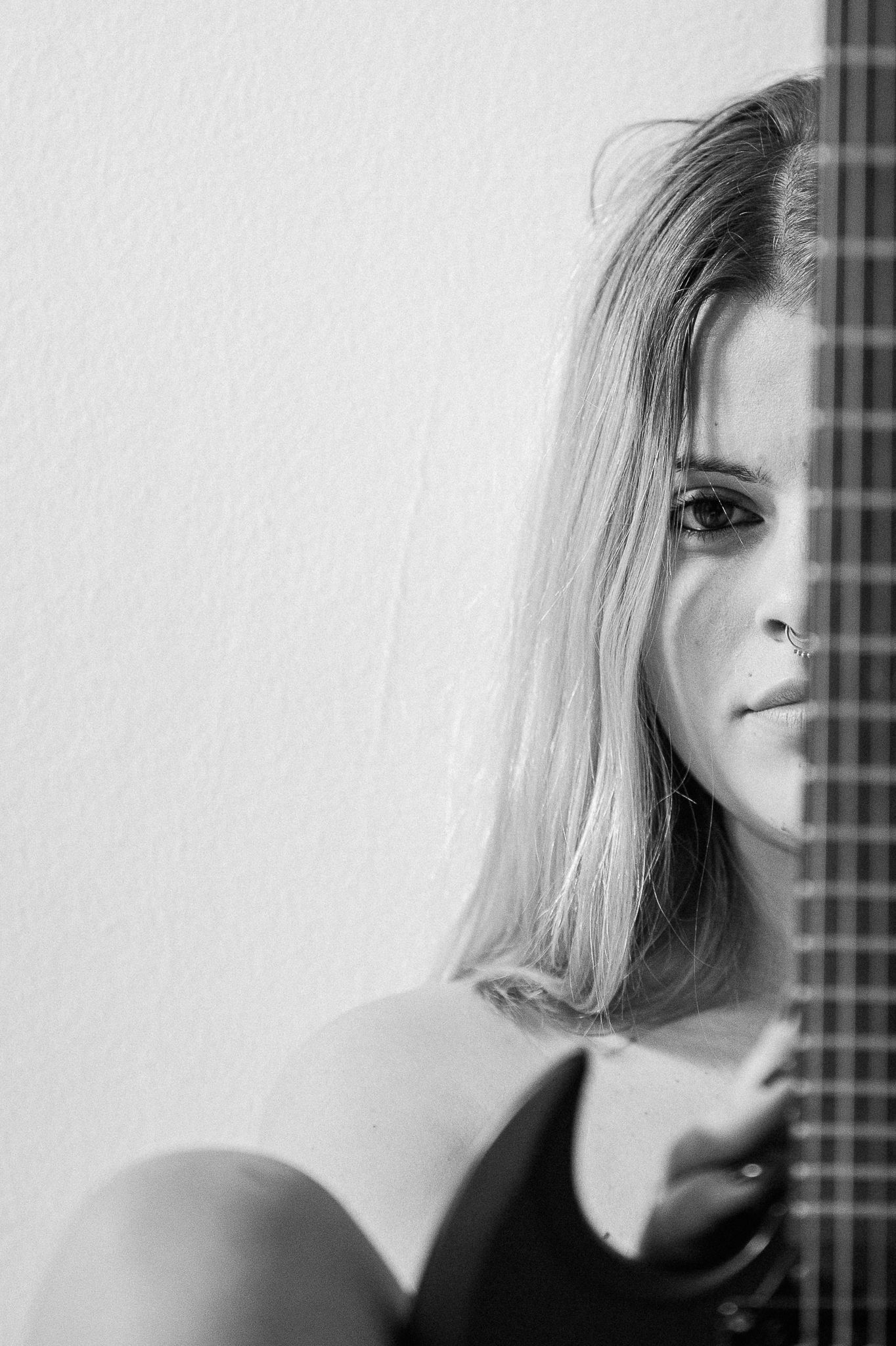 Artistic black and white portrait with guitar neck visible against white wall.