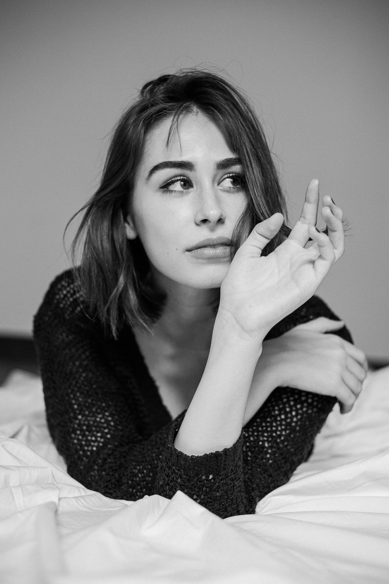 Black and white photo series showing a person lying down in a dark sweater against white bedding making playful expressions.