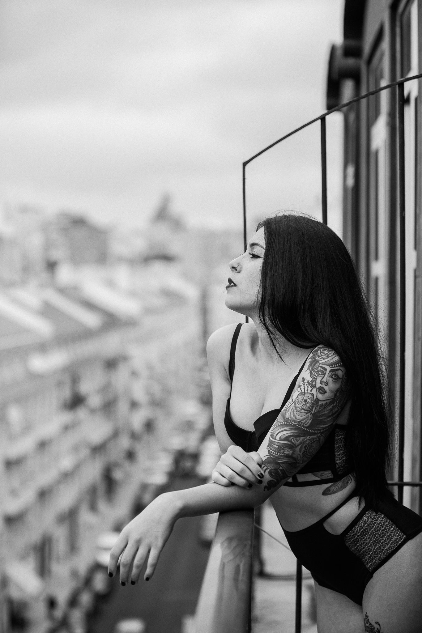Black and white portrait of a woman in lingerie looking out over a cityscape from a balcony.