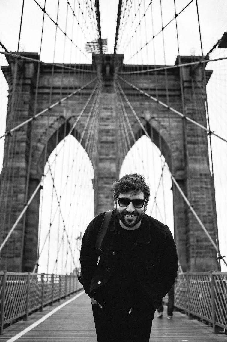 Person in black clothing walking across the iconic Brooklyn Bridge in black and white.