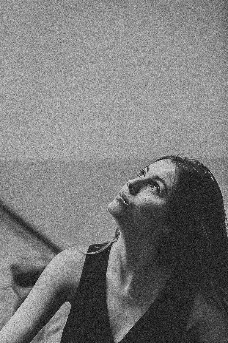 Dramatic black and white portrait of a woman in a dark top looking upward with contemplative expression.