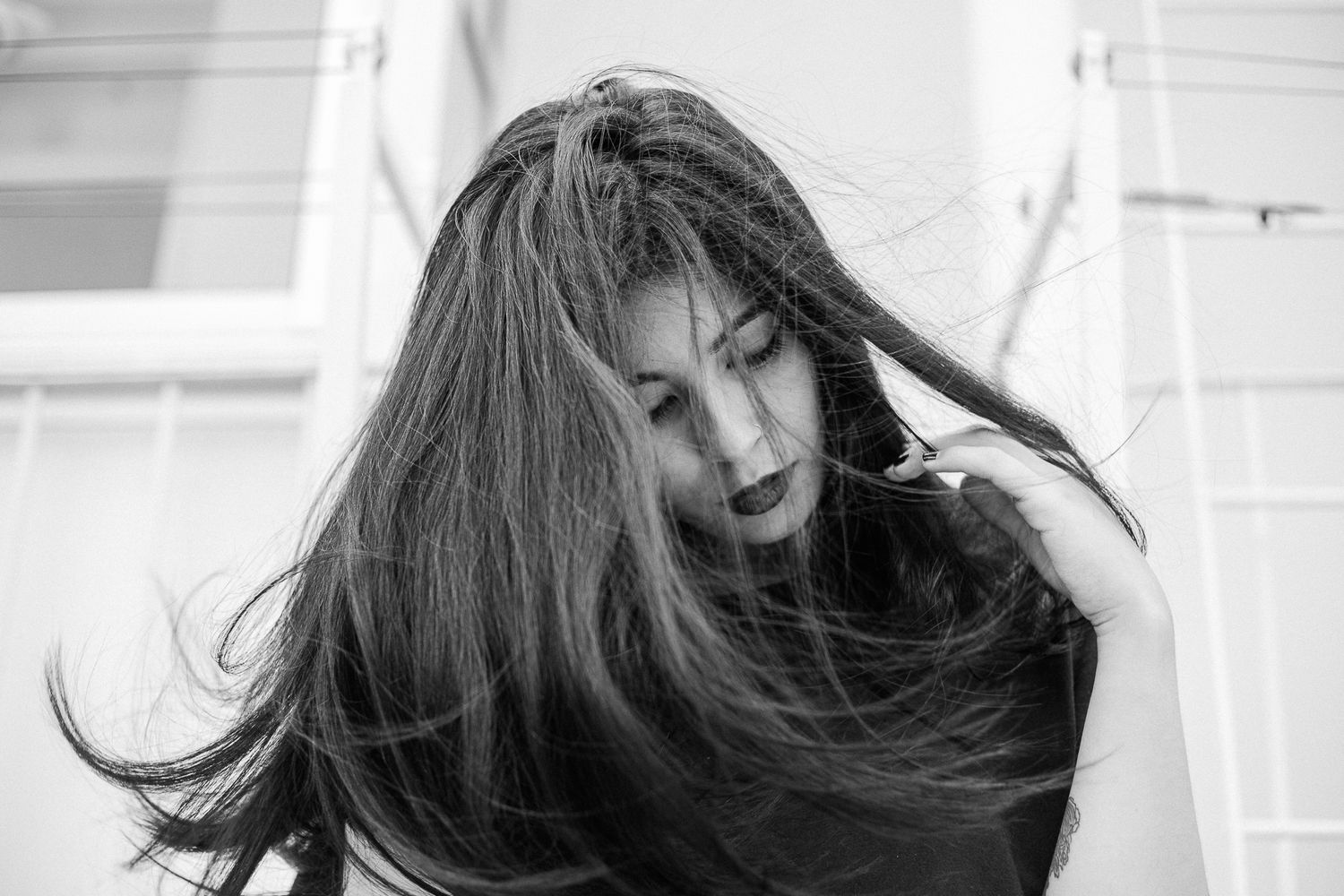 Long dark hair flows dramatically against a minimalist black and white architectural backdrop.